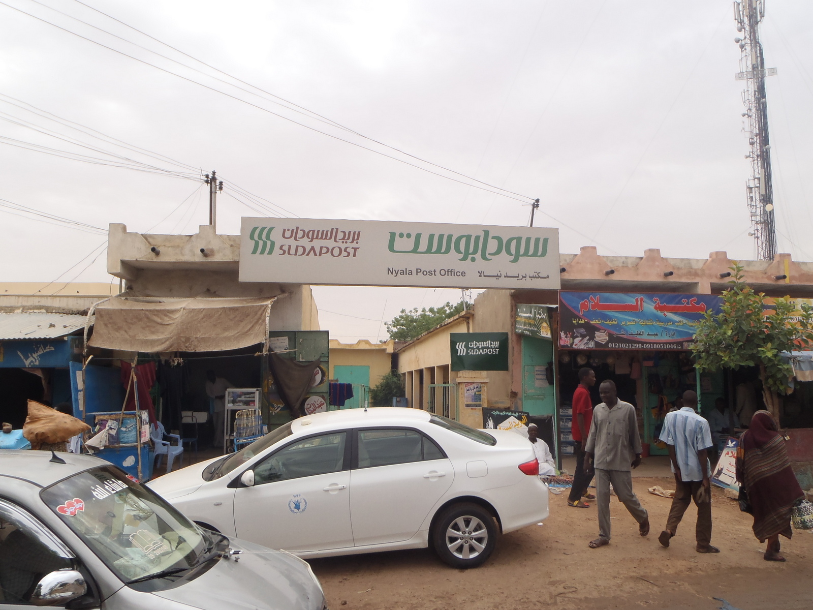 A street in Nyala, Sudan, with the post office sign, parked cars and people walking