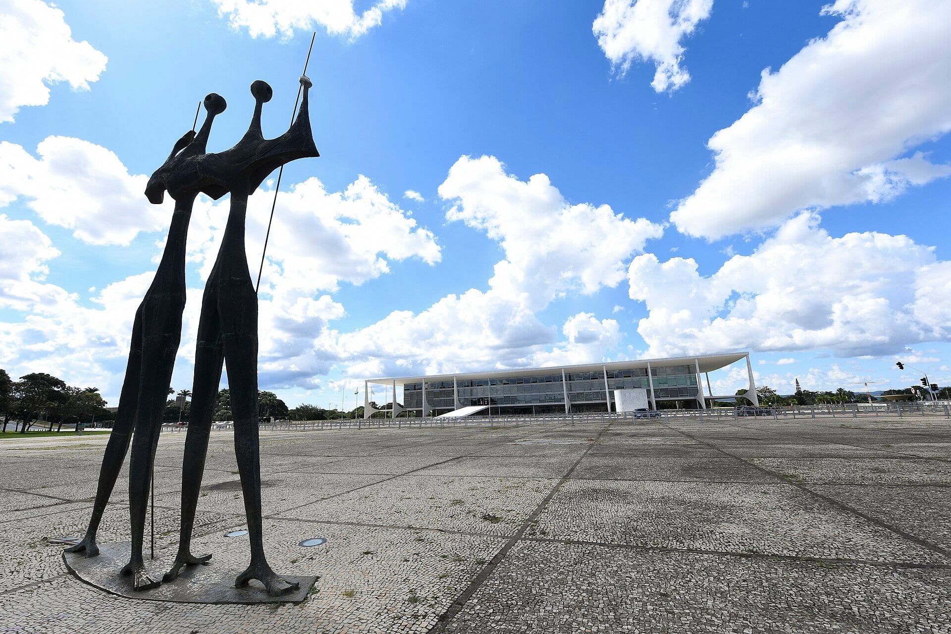Bronze Candangos statue on the paved Three Powers Square in Brasilia with the presidential palace under a blue sky