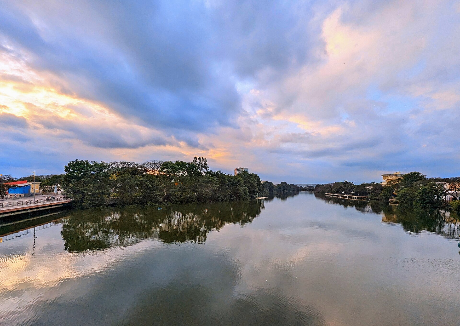 A calm tidal creek reflecting trees and a dusk sky, with a walkway on the left bank in Guayaquil