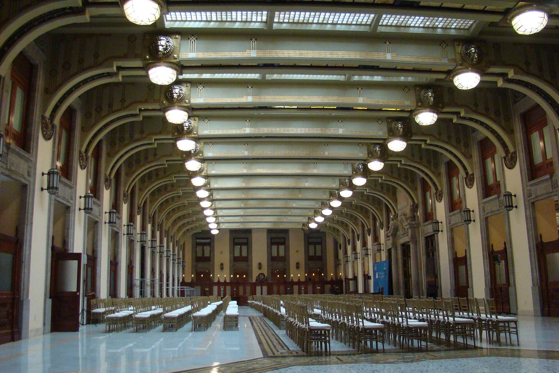 Long hall with arched ceiling, hanging lamps and rows of chairs in the National Palace, Mexico City