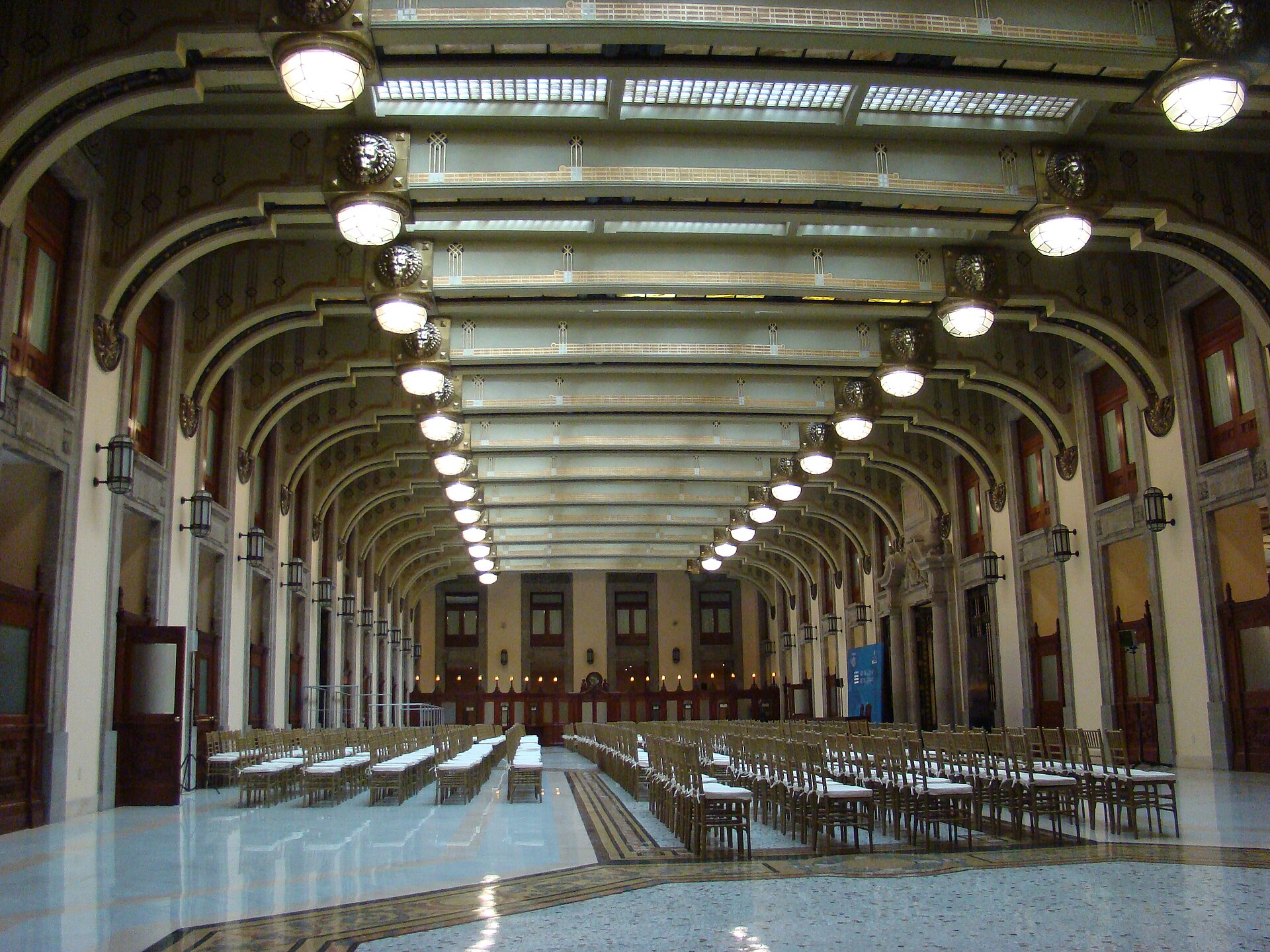 Long hall with arched ceiling, hanging lamps and rows of chairs in the National Palace, Mexico City