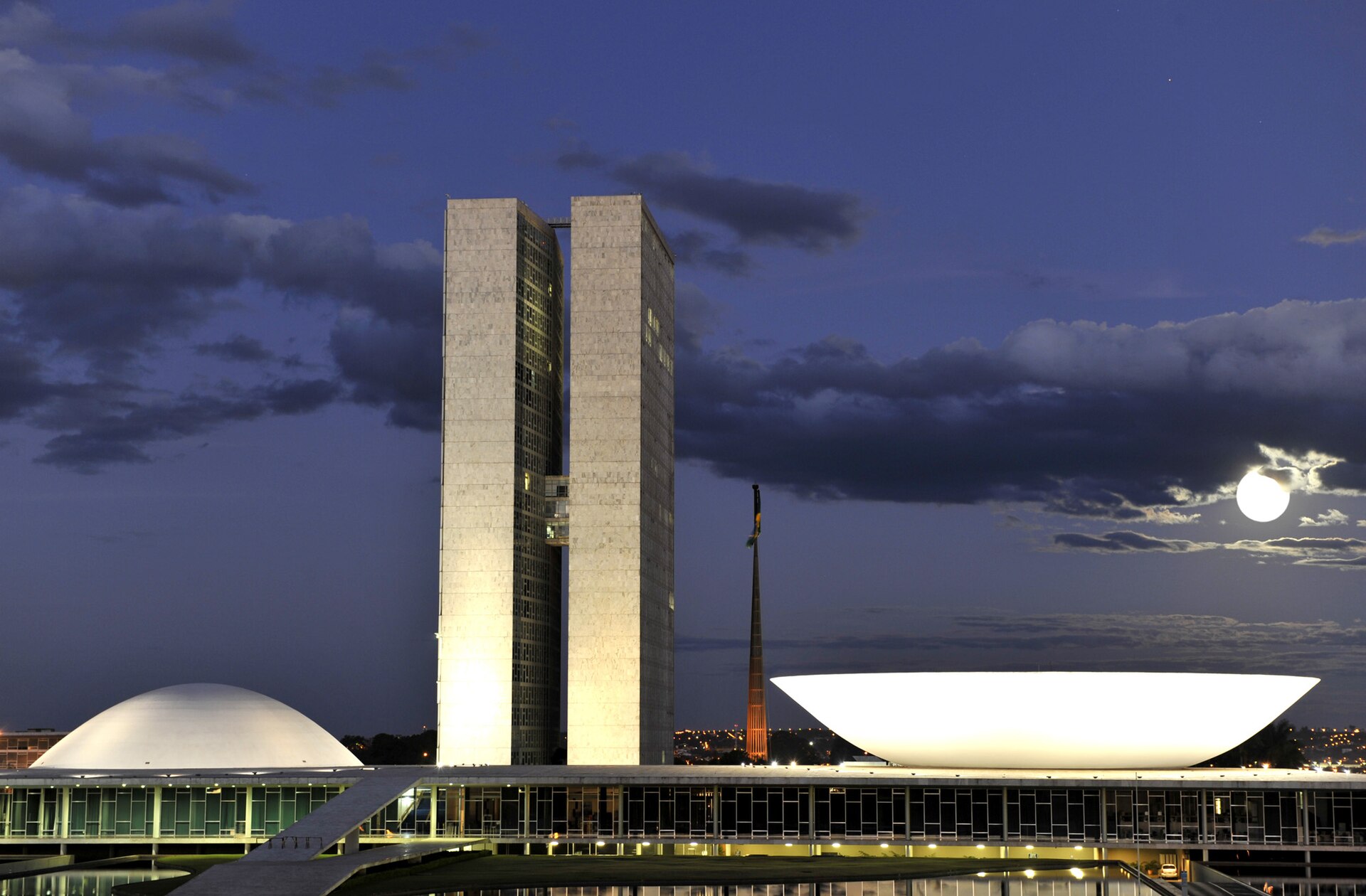 The twin towers and two domes of Brazil's National Congress in Brasilia at dusk with a full moon beside a dark cloud
