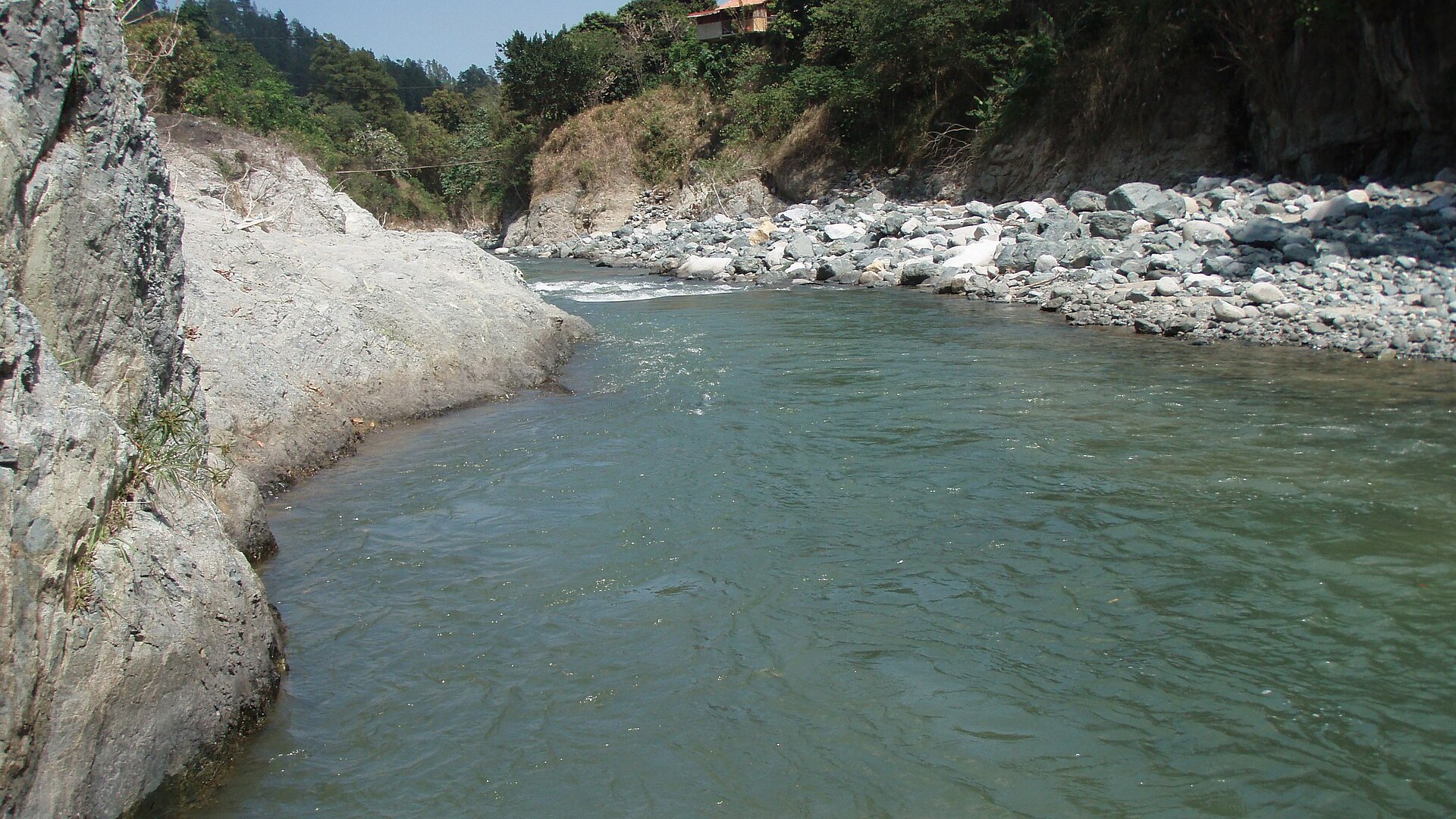 The Yaque del Norte river near Jarabacoa, Dominican Republic, running between rock walls and a stony bank