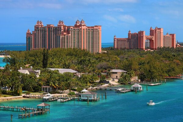 Pink towers of the Atlantis resort on Paradise Island, Nassau, rising above palm trees and turquoise water, with small docks and a motorboat in the foreground.