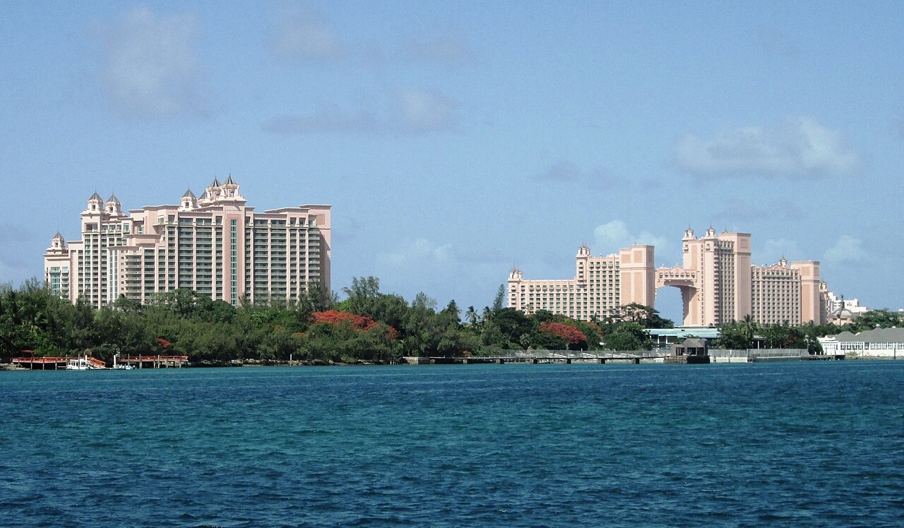 The two pink Atlantis towers on Paradise Island seen across the blue water of Nassau harbour, with green trees along the shore.