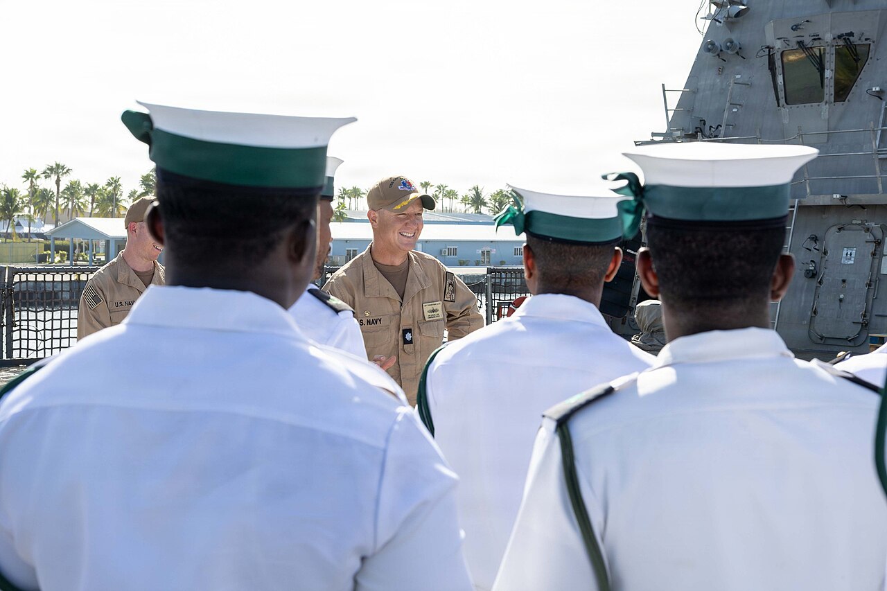 A US Navy commander talks with Royal Bahamas Defence Force sailors in white uniforms on the deck of a US Navy ship at Freeport