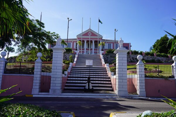 Government House in Nassau, a pink colonial-style building at the top of a wide flight of steps, with the Bahamian flag flying above it