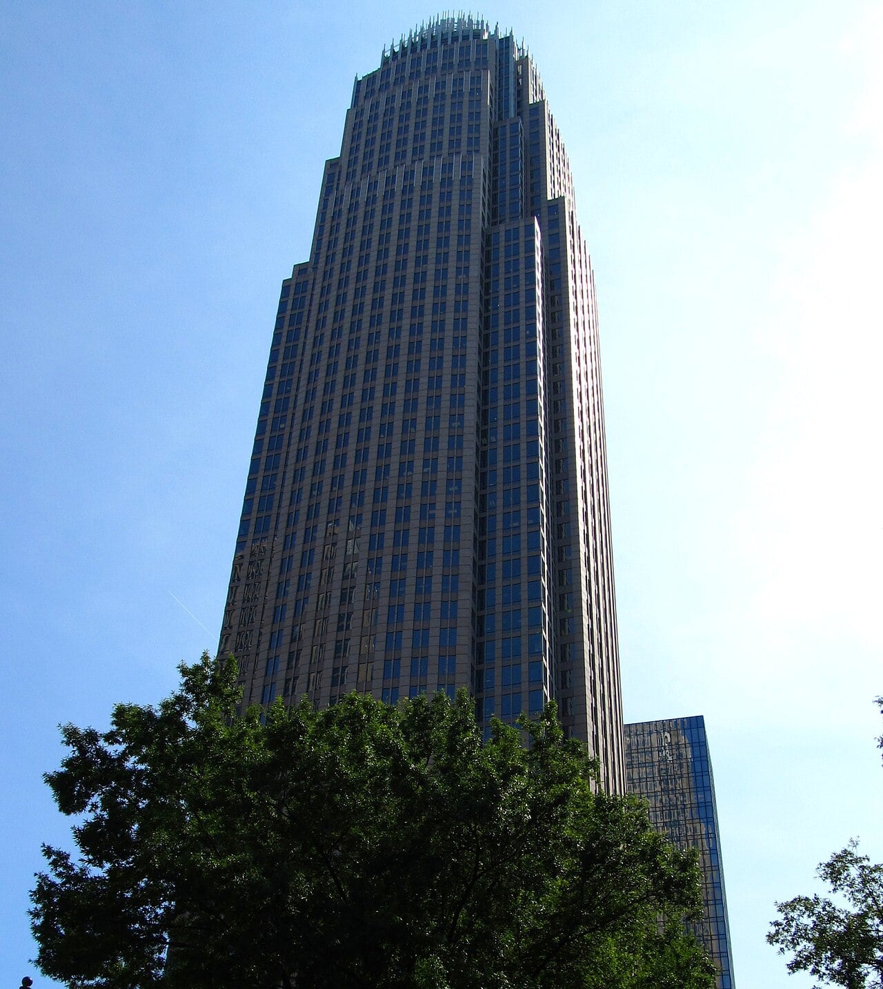 The dark glass Bank of America Corporate Center tower rising above green trees against a blue sky in Charlotte, North Carolina