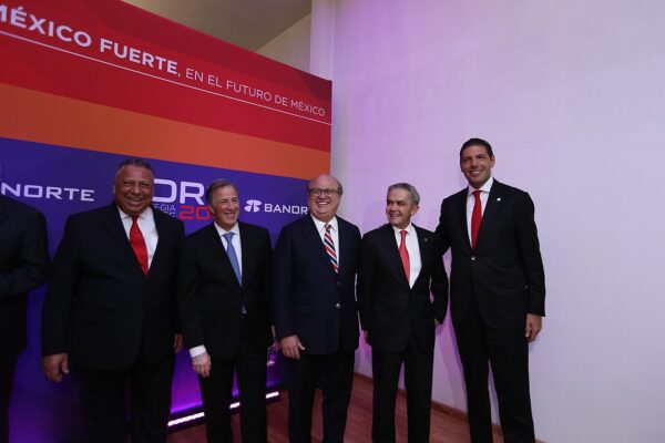 Five men in dark suits stand smiling in front of a Banorte-branded backdrop at a business forum