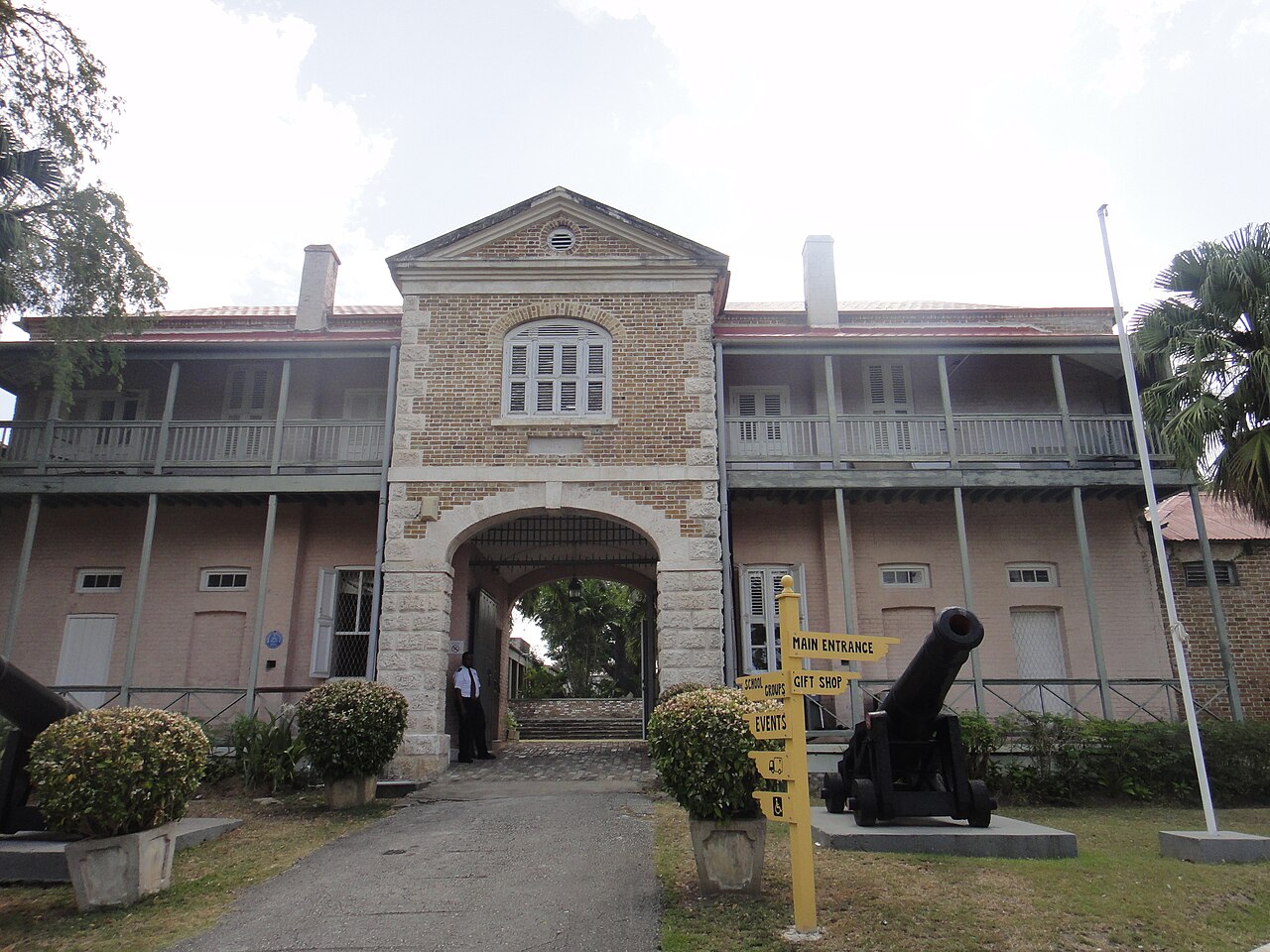Two-storey brick garrison building with an arched gateway, wooden balconies and an old cannon in the grounds