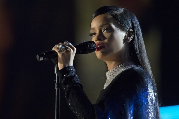 Singer Rihanna performing on stage, holding a microphone, in a sequinned dark outfit