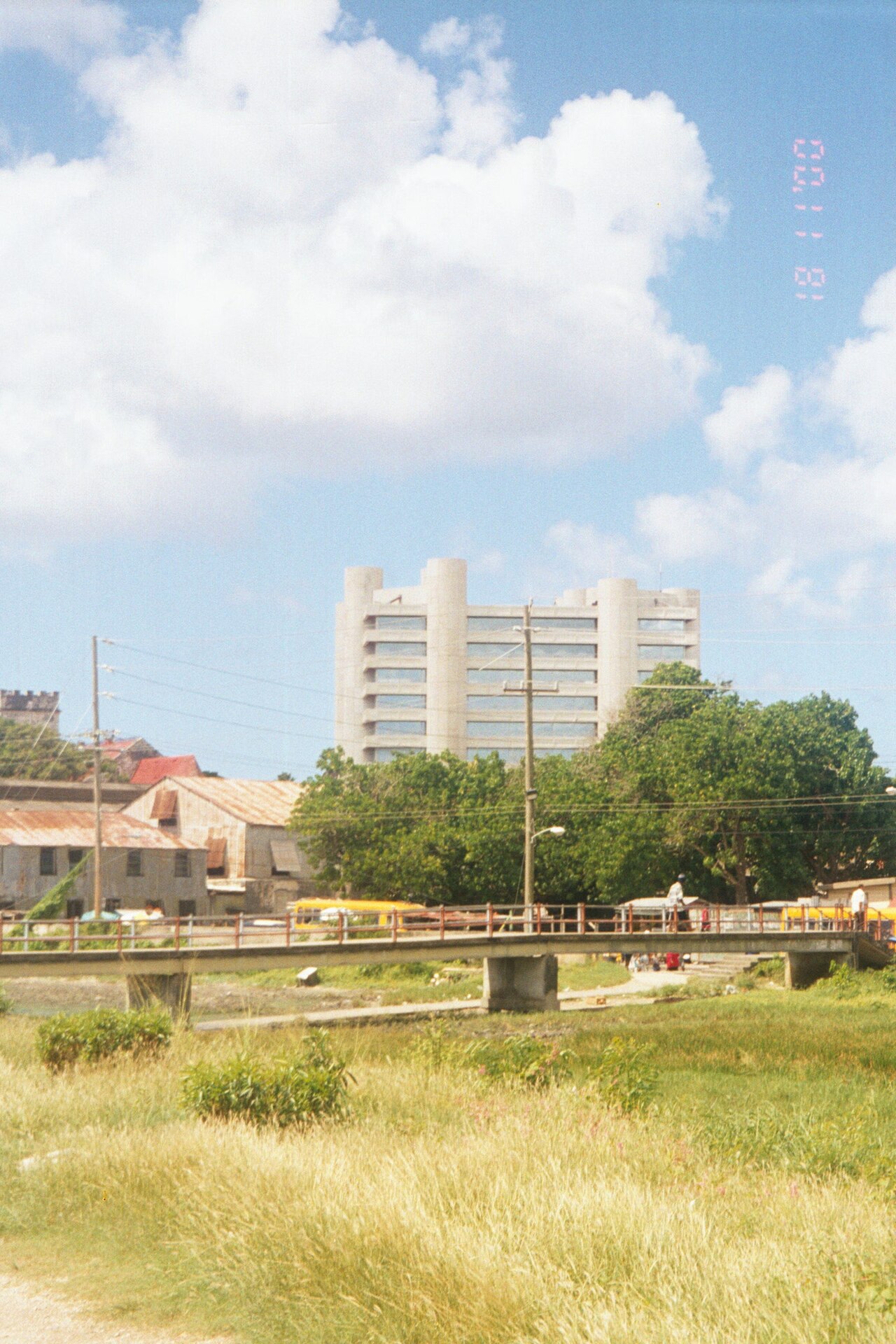 The concrete Central Bank of Barbados tower with rounded corner towers, seen over trees and a footbridge in Bridgetown.