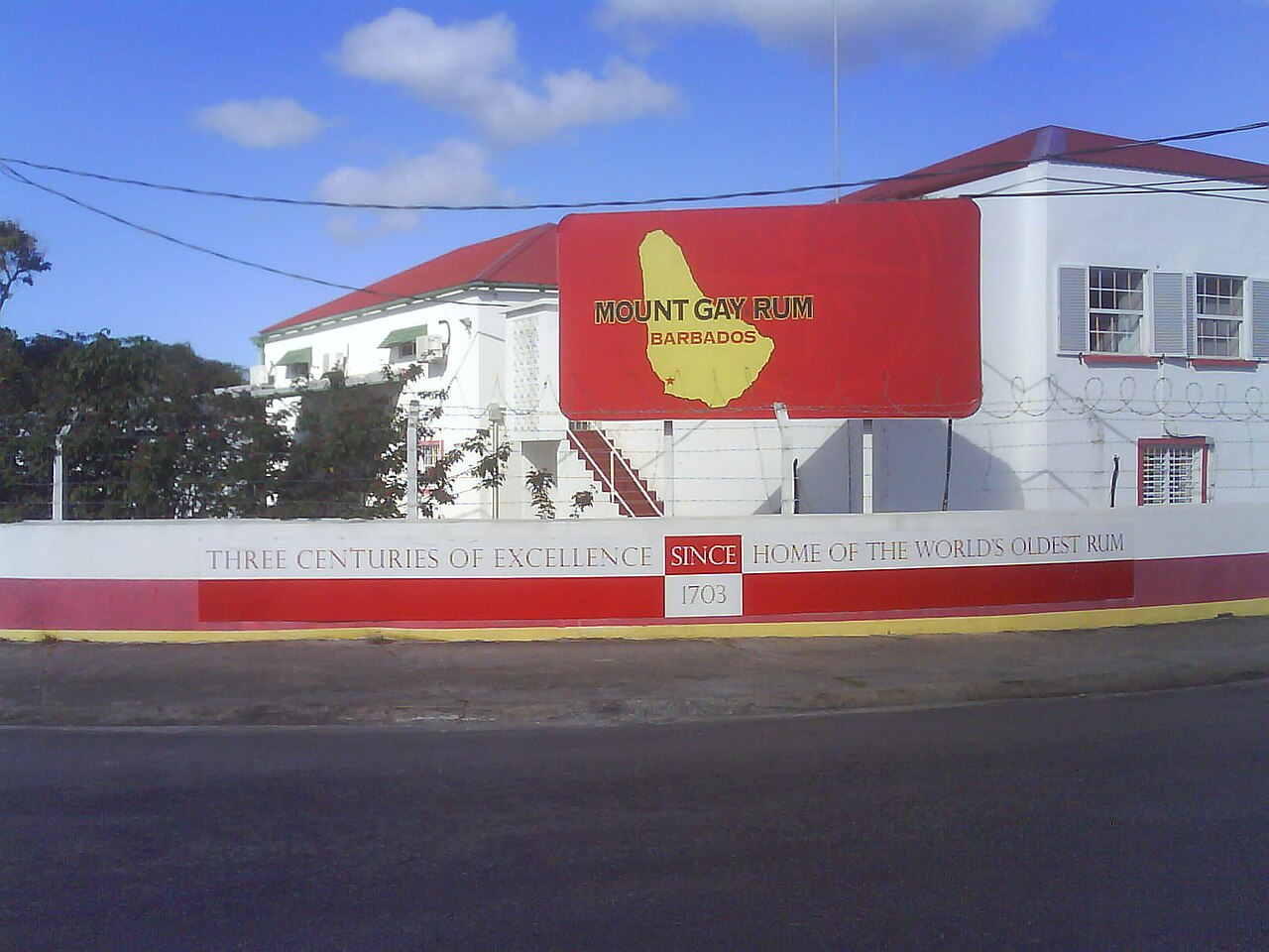 Red Mount Gay Rum billboard on a white building with a wall reading Three Centuries of Excellence, Since 1703, Home of the World's Oldest Rum.