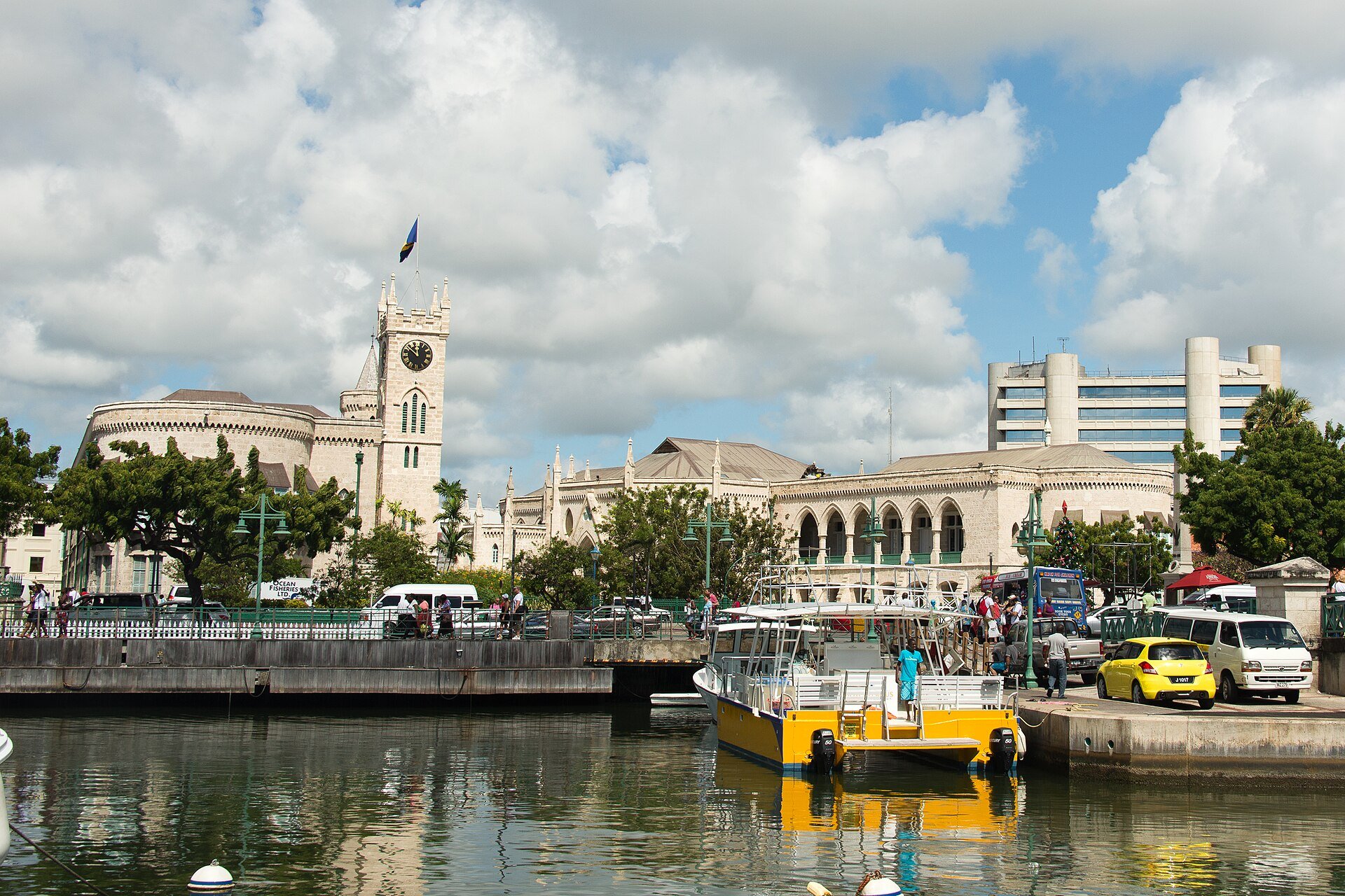 The stone Parliament Buildings with a clock tower in Bridgetown, Barbados, seen across the water with a yellow tour boat in front