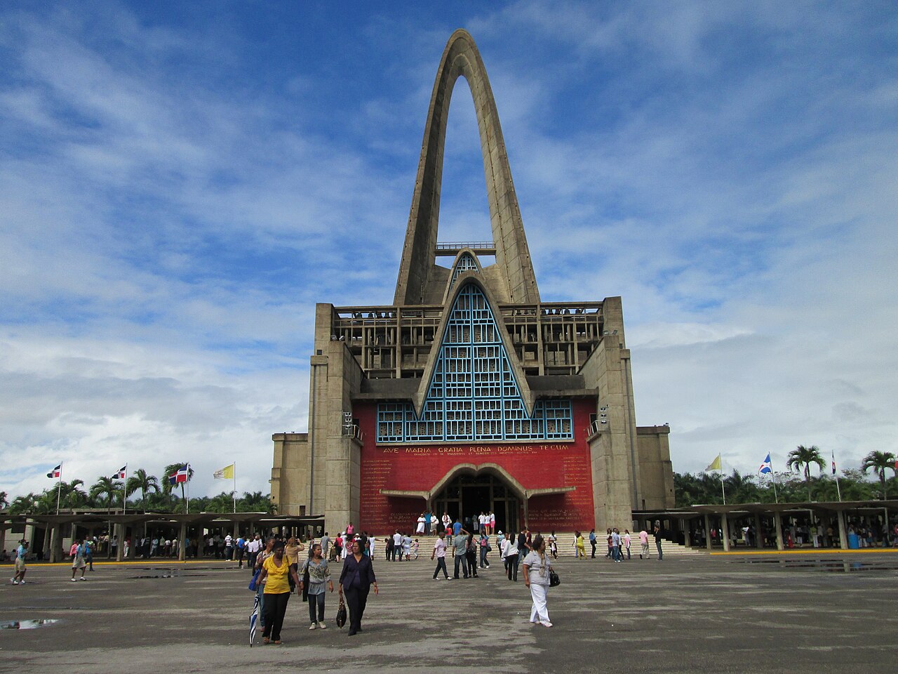 The Basilica of Our Lady of Altagracia in Higüey, Dominican Republic, with its tall concrete arch and visitors on the plaza.