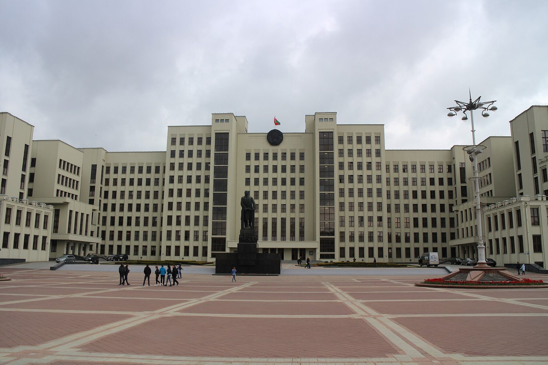 The House of Government in Minsk, with the Belarusian flag above the entrance and a statue in front of the building