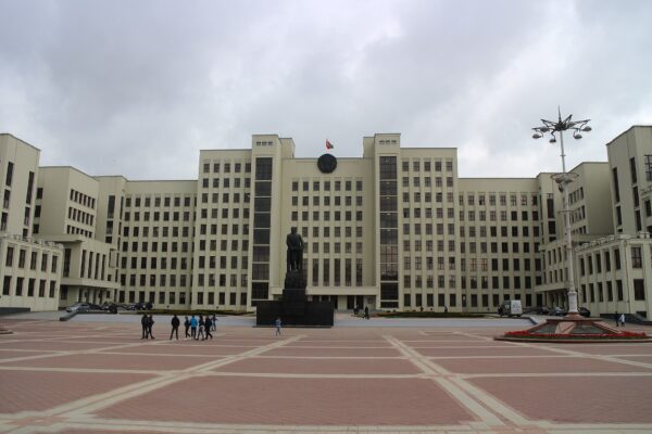 The House of Government in Minsk, with the Belarusian flag above the entrance and a statue in front of the building