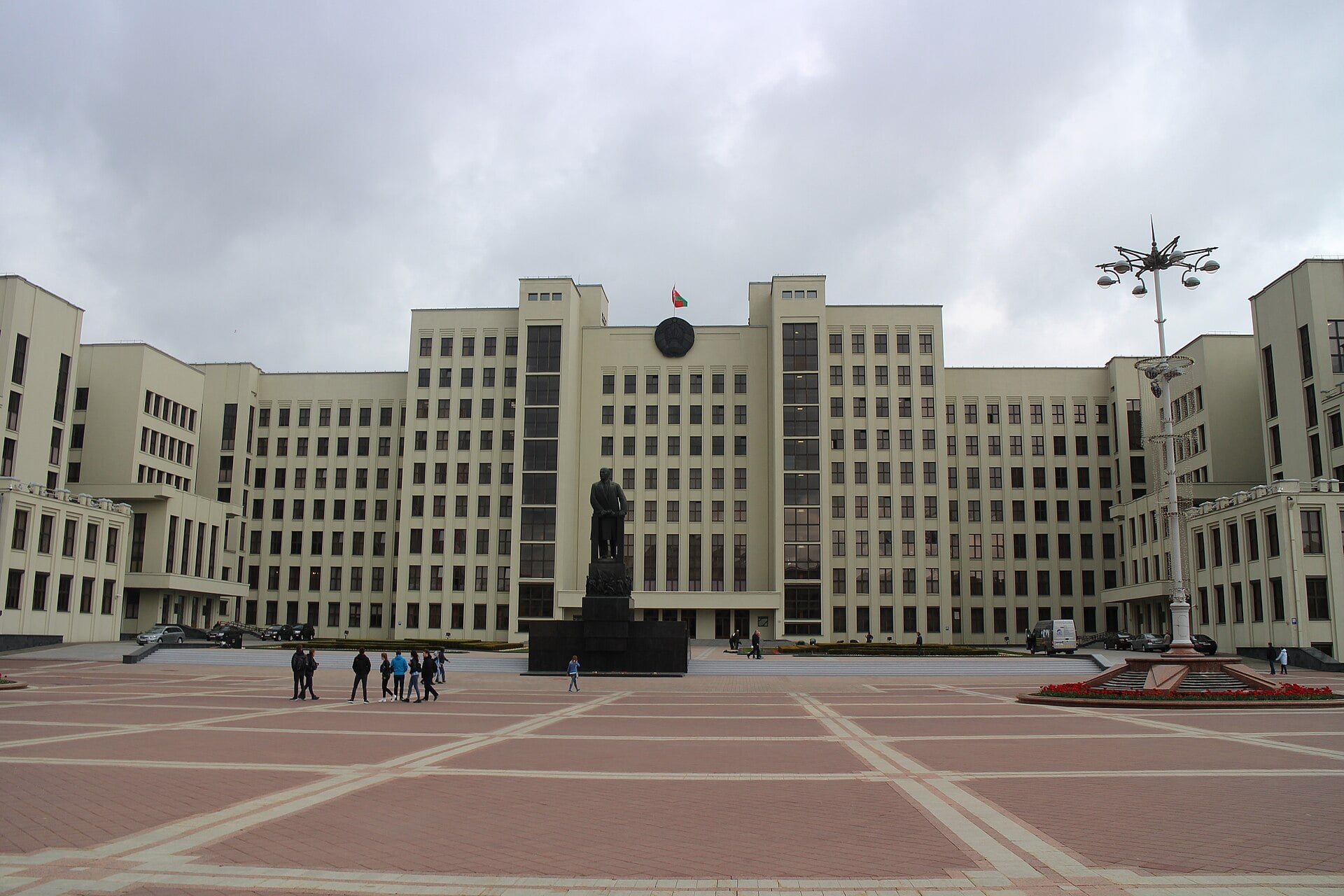 The House of Government in Minsk, with the Belarusian flag above the entrance and a statue in front of the building