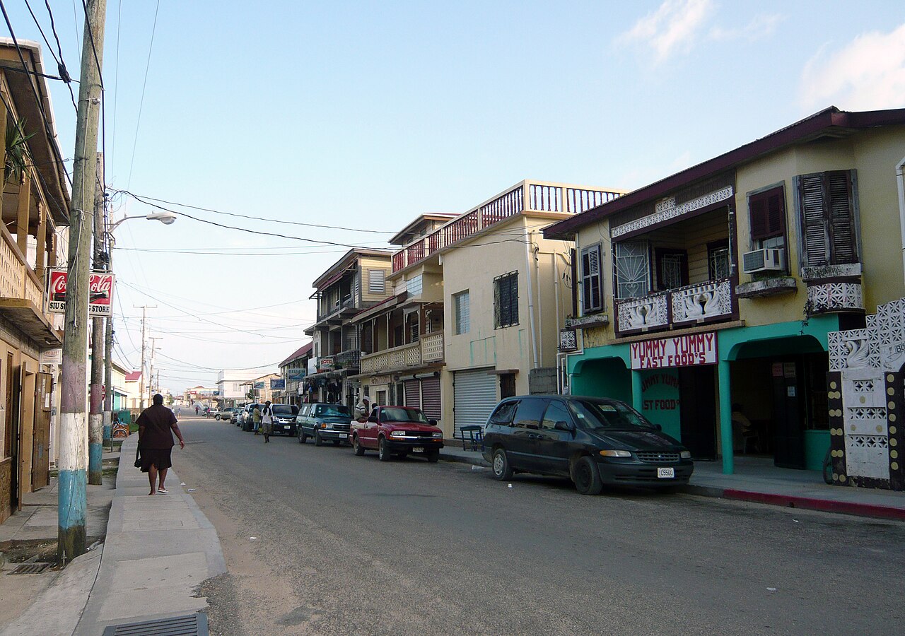Main street of Dangriga, Belize, lined with two-storey wooden and concrete buildings and parked cars