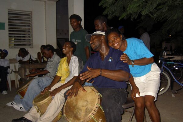 Garifuna drummers playing large hand drums at night with a woman leaning over a drummer's shoulder in Belize