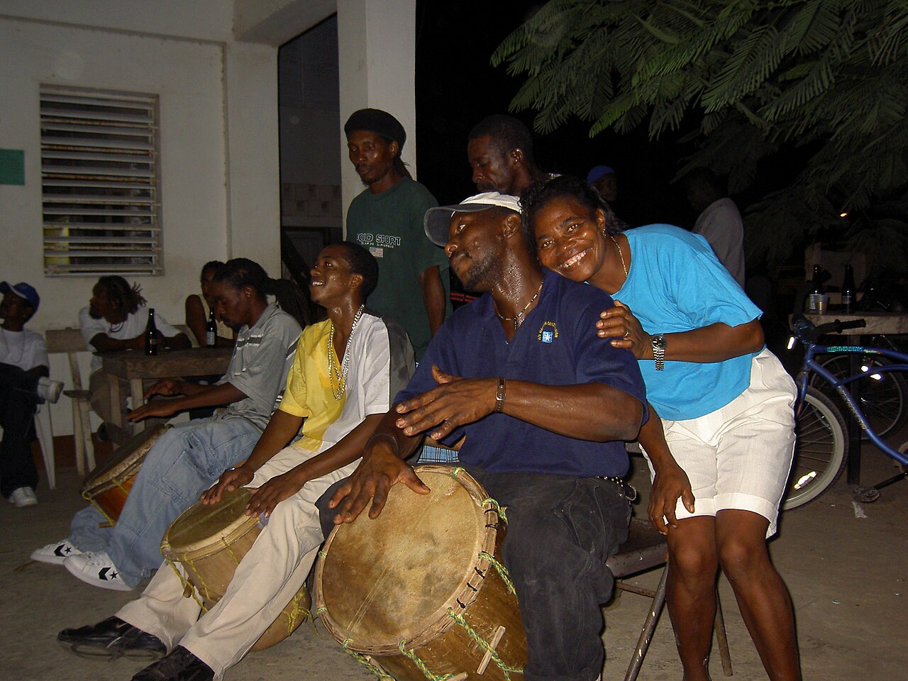 Garifuna drummers playing large hand drums at night with a woman leaning over a drummer's shoulder in Belize