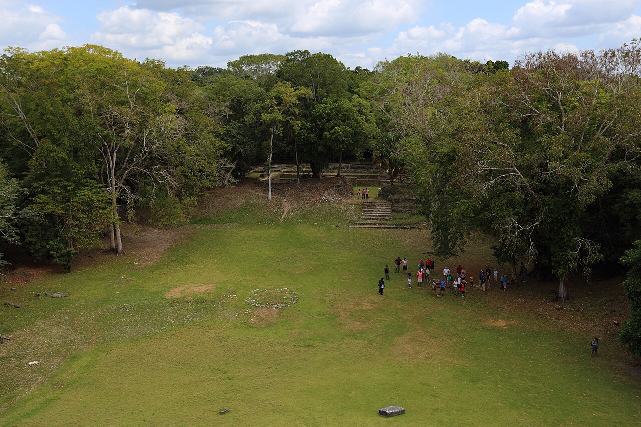 Grassy plaza surrounded by forest at the Maya site of Lamanai in northern Belize, with visitors gathered below