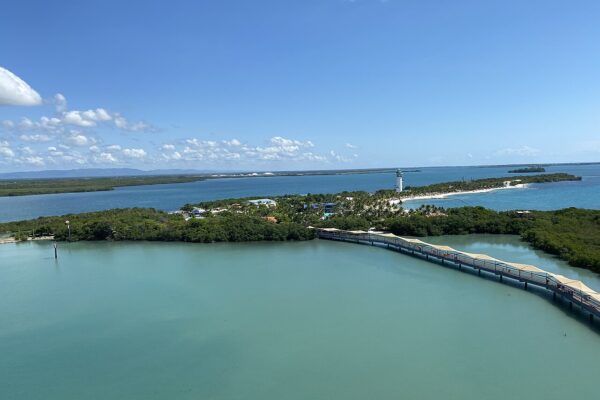 Harvest Caye cruise port in southern Belize, with a white lighthouse, a beach and a covered walkway over the water