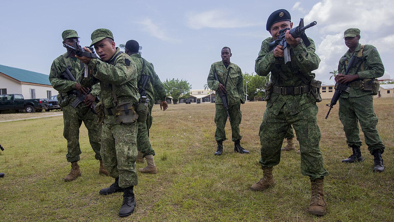 Belize Defence Force soldiers in camouflage practise rifle drills on a grass field during a US-led training course.