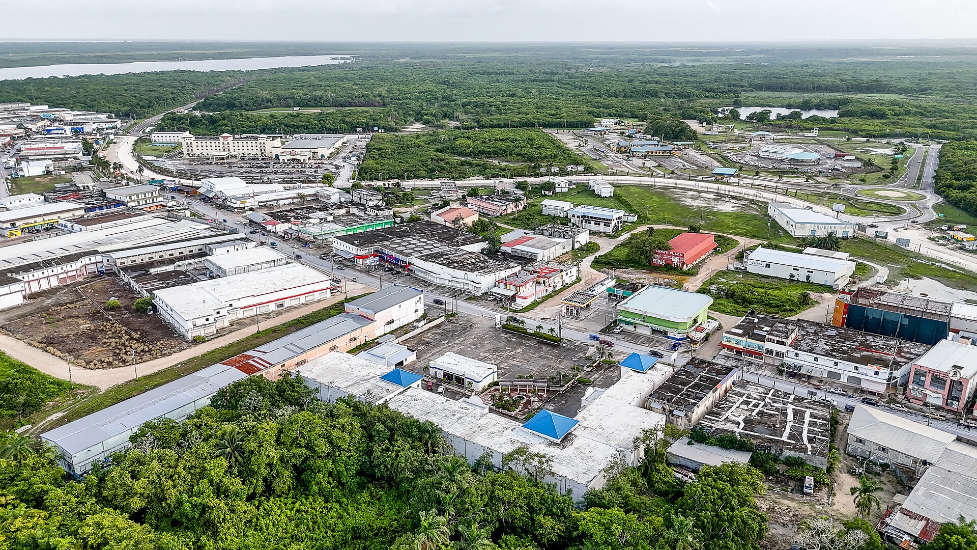 Aerial view of warehouses, shops and roads of the Corozal Free Zone at Santa Elena, with forest and open water in the distance