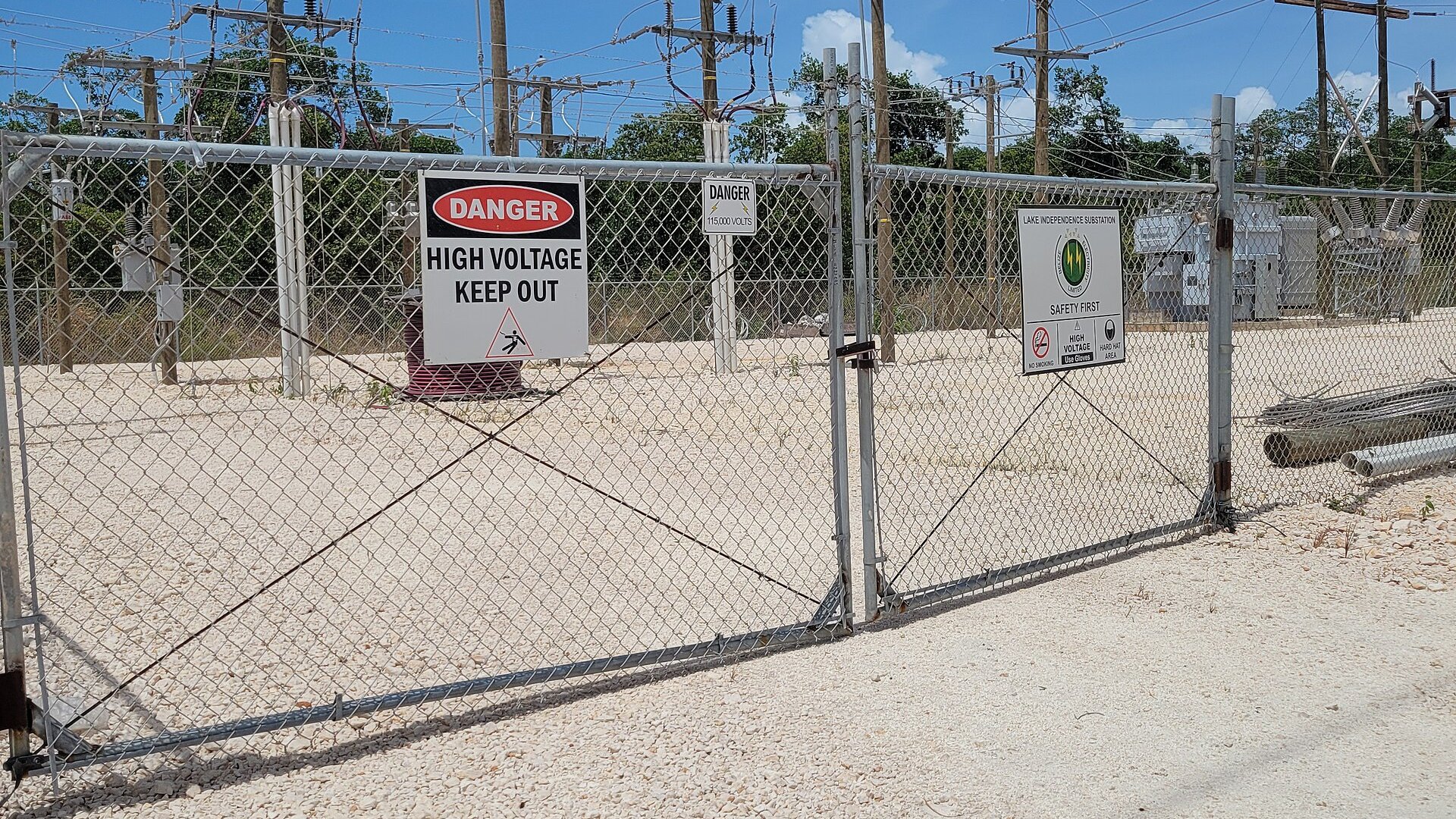A fenced Belize Electricity Limited high-voltage substation with danger signs and transformers
