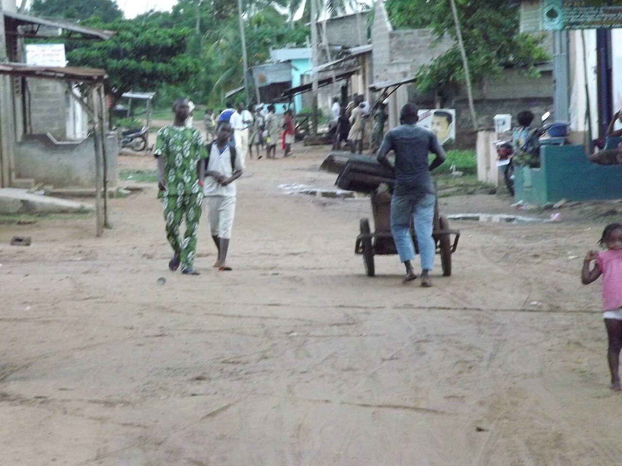 Dirt street with pedestrians and a man pushing a handcart in a neighbourhood of Cotonou, Benin