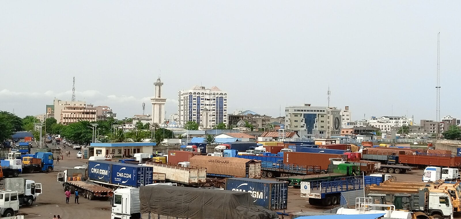 Trucks and shipping containers in a freight yard with city buildings behind in the Zongo district of Cotonou, Benin