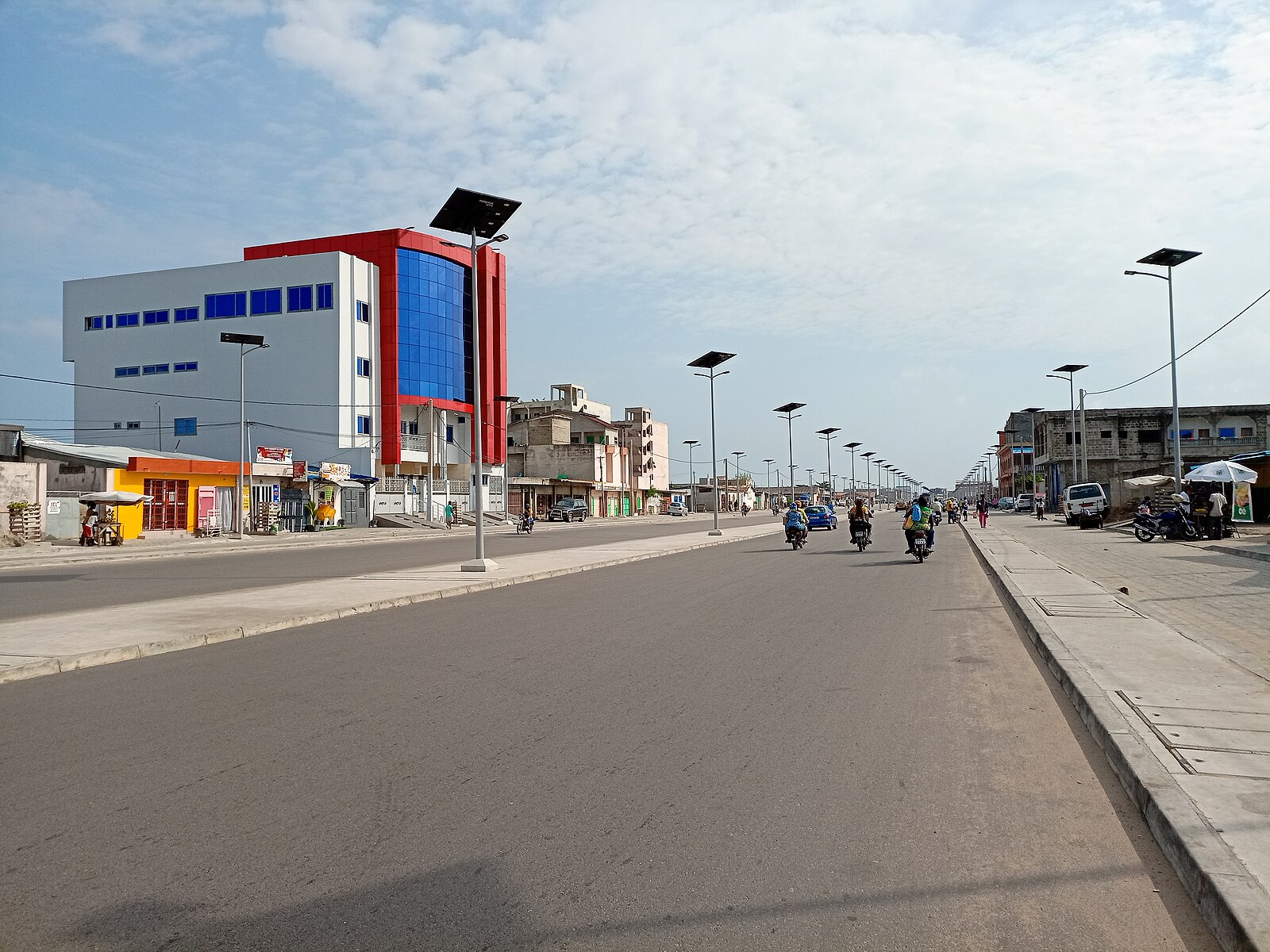 A wide road with solar street lamps and motorbikes in the Agontikon district of Cotonou, Benin