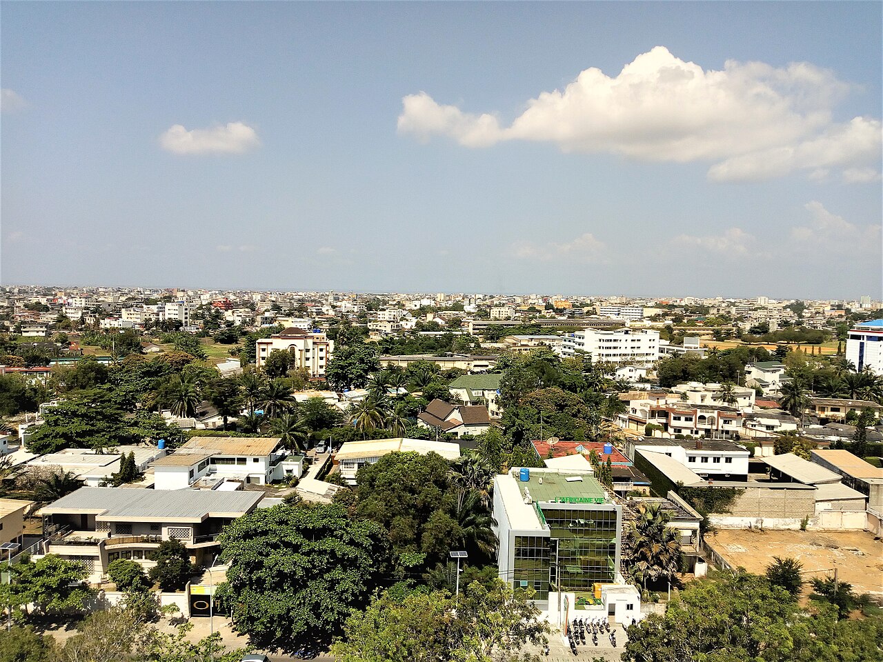 Rooftops, palm trees and low buildings of Cotonou, Benin's largest city, under a blue sky