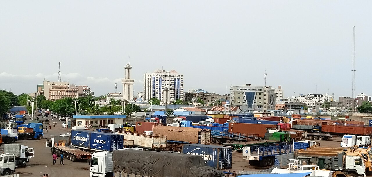 Container trucks parked in a lot in Cotonou with a minaret and office buildings behind
