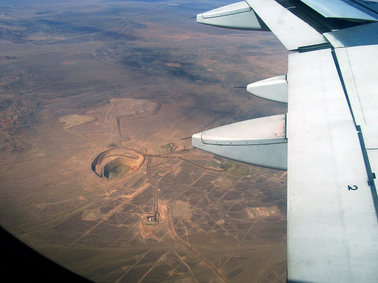 Aerial view of an open-pit copper mine and its access roads in the desert of Chile's Antofagasta Region, seen past an aircraft wing