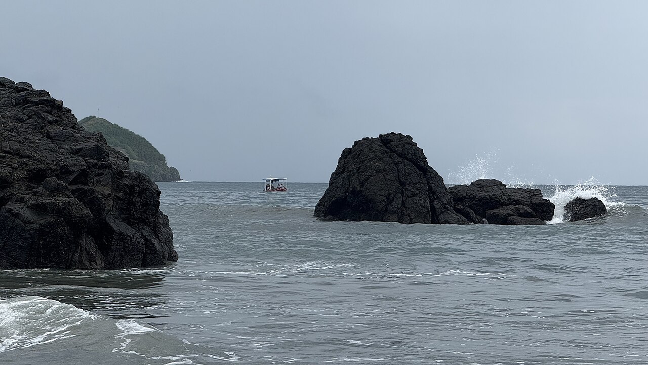 A small boat beyond dark rocks and breaking waves on the Pacific coast at Manuel Antonio, Costa Rica.
