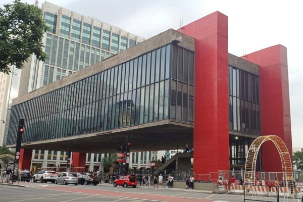 The red concrete frame and glass hall of the MASP art museum on Avenida Paulista in São Paulo, with pedestrians and cars on the street below.