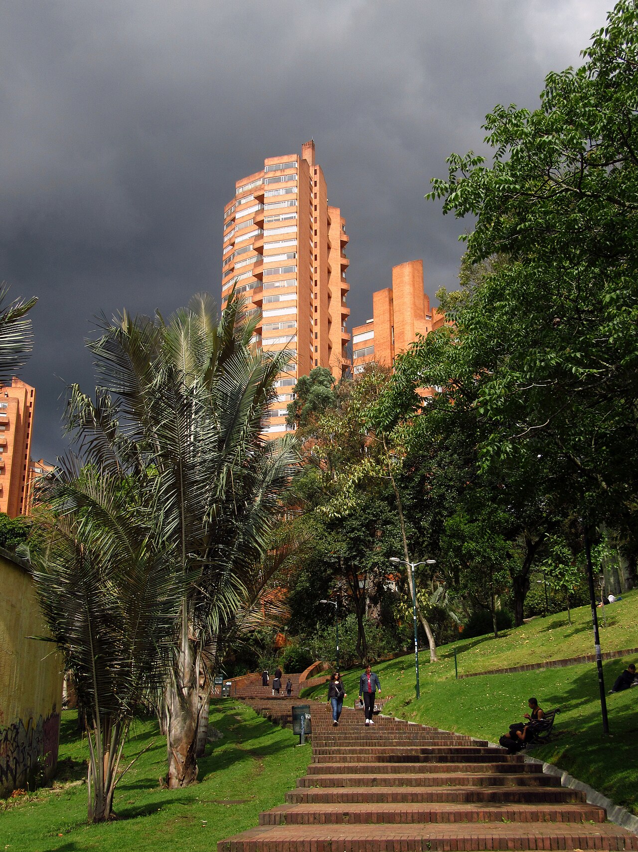 Brick towers of Torres del Parque rise above trees and a stairway in Parque de la Independencia, central Bogotá, Colombia