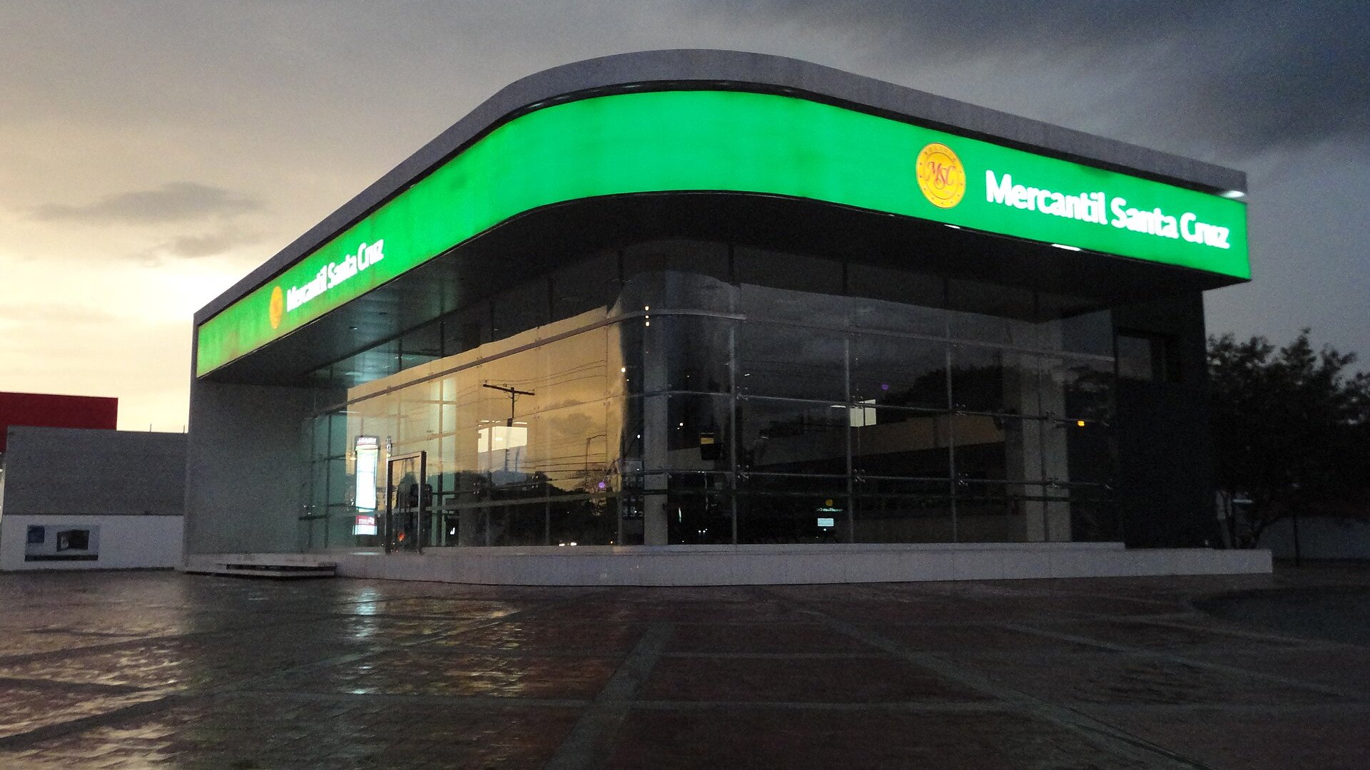 Illuminated glass branch of Banco Mercantil Santa Cruz at dusk in Santa Cruz, Bolivia