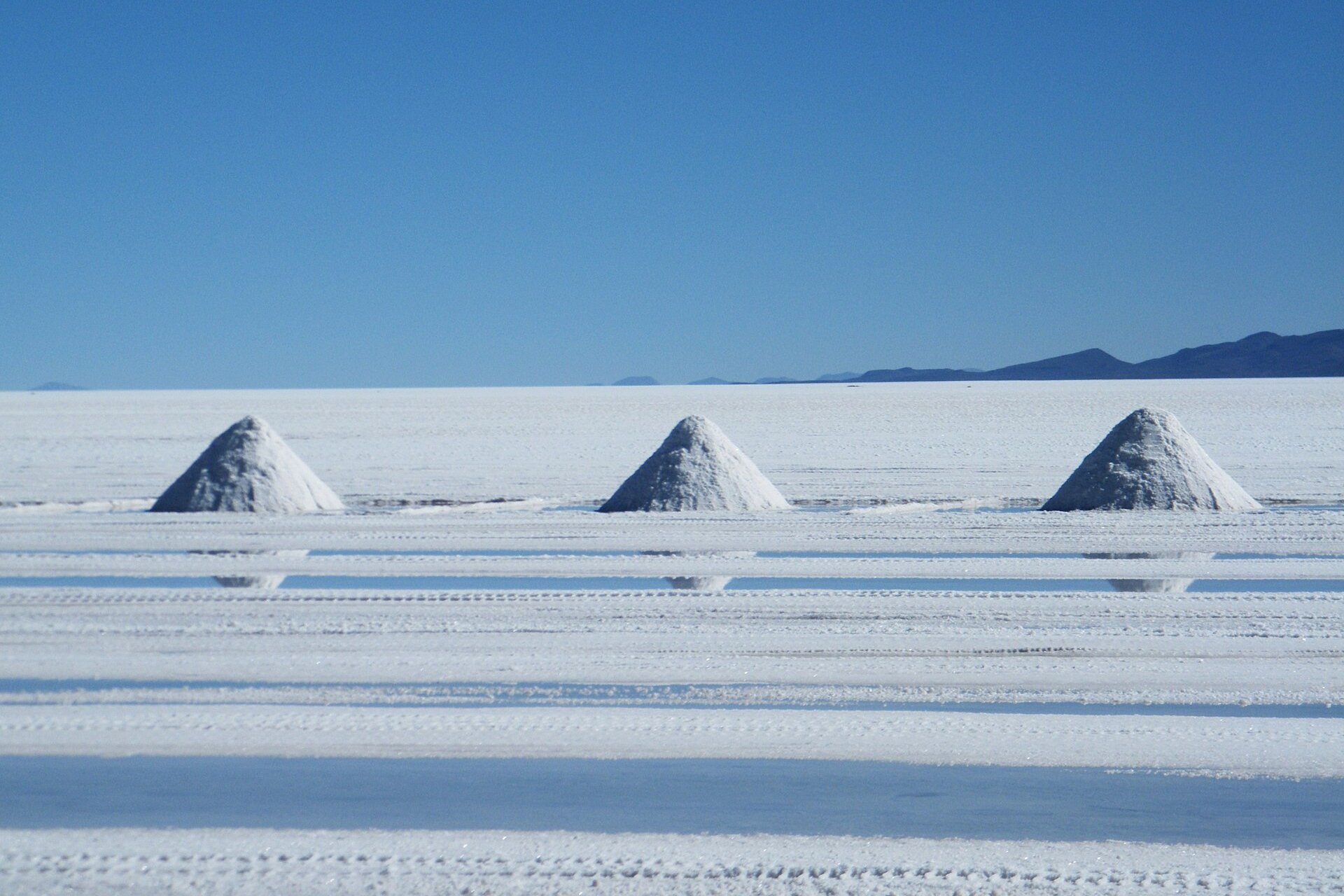 Three cones of white salt on the flat surface of the Salar de Uyuni under a deep blue sky, with low mountains on the horizon
