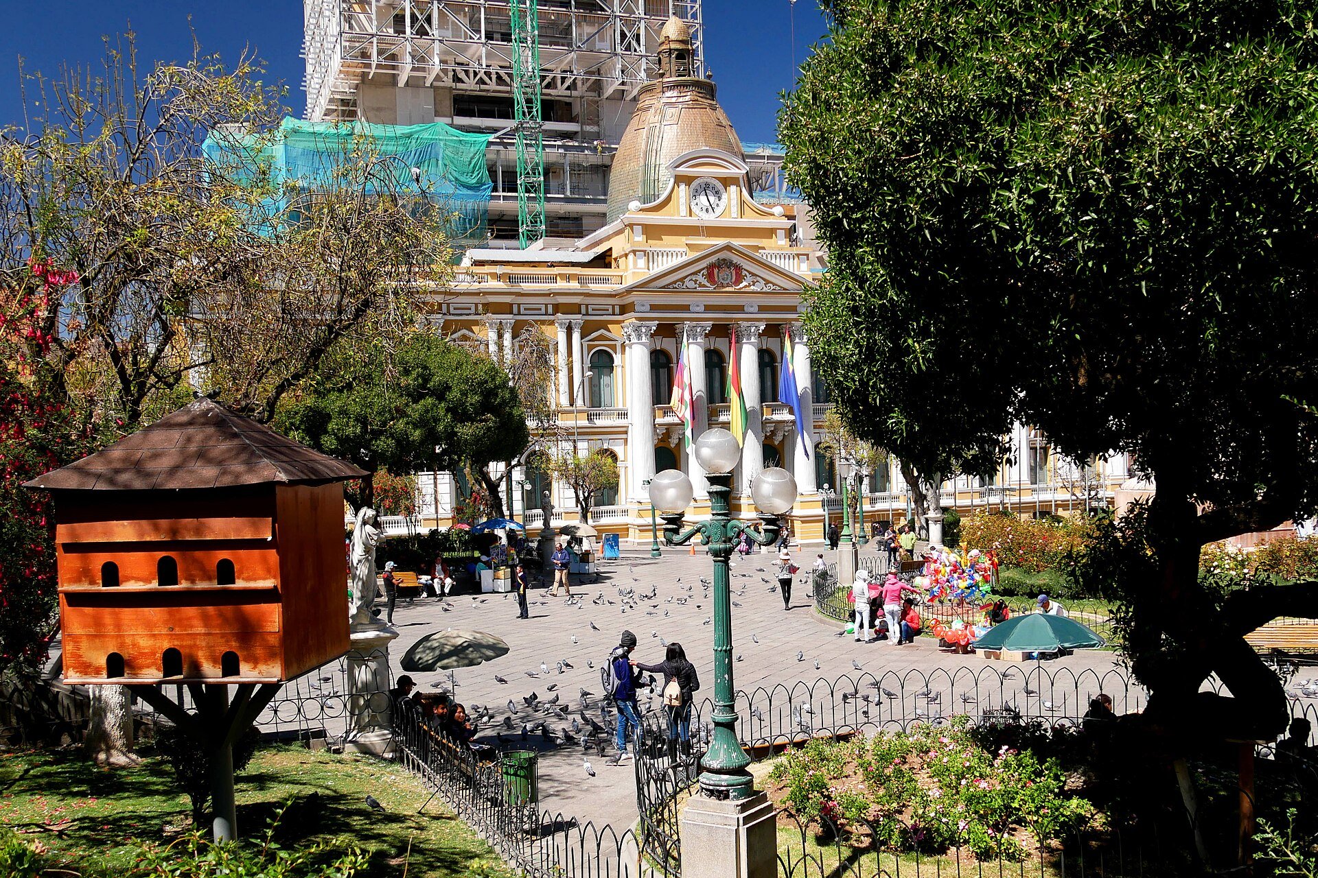 Plaza Murillo in La Paz with a yellow neoclassical government building, flags, pigeons and visitors in the square