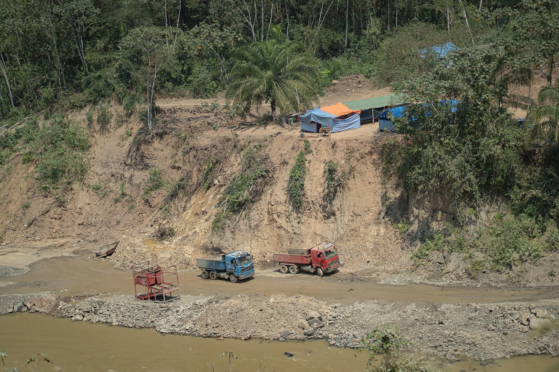 Dump trucks and makeshift camps beside a gold-mining site on the Mapiri River in Bolivia