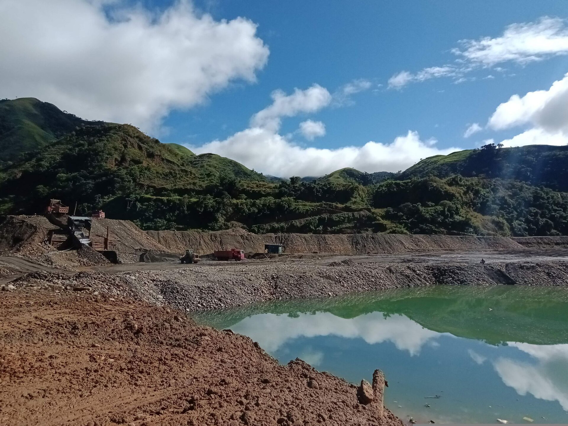 A tailings pond from alluvial gold mining near the Tipuani River in Bolivia with trucks and machinery behind