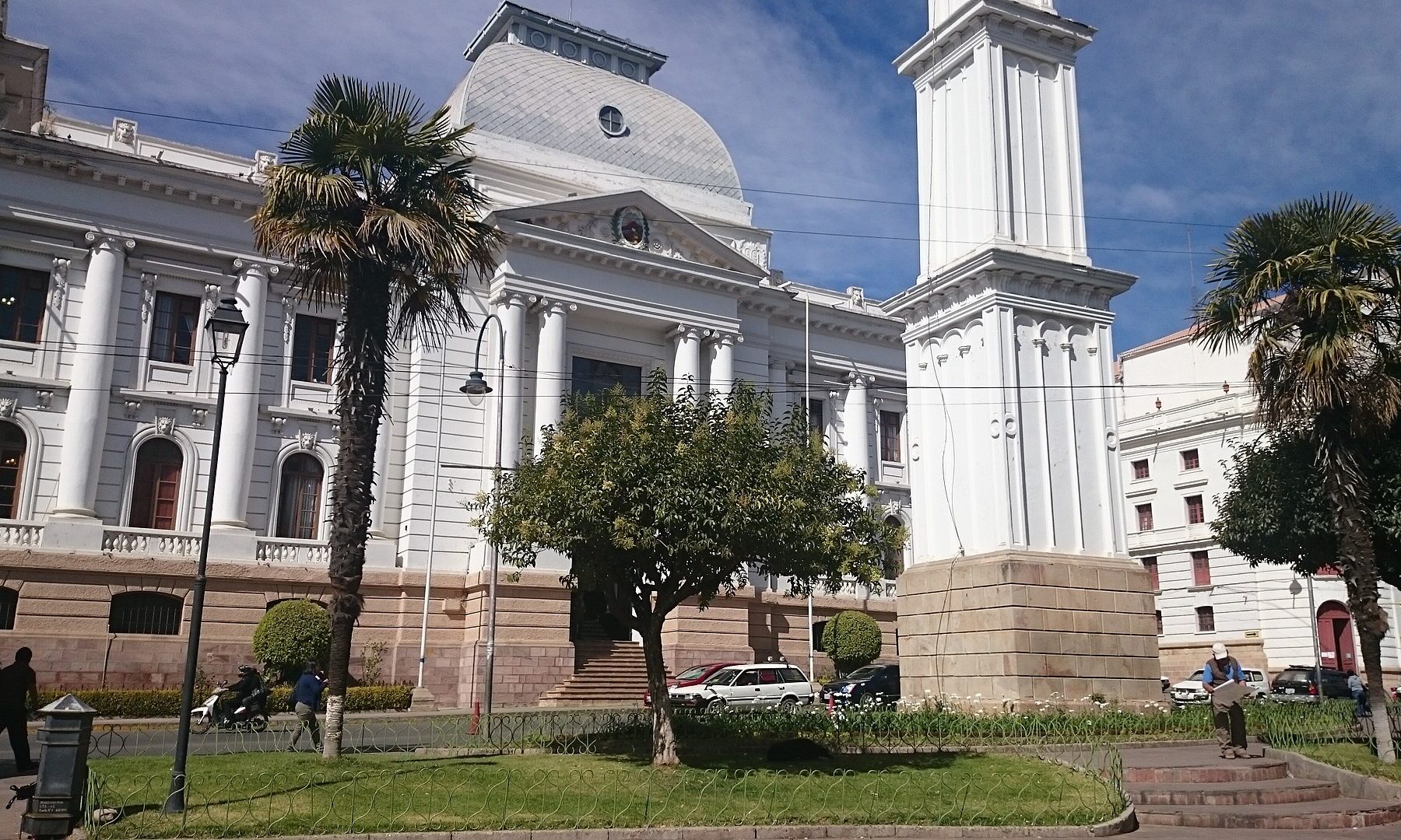 Neoclassical palace with a dome and a white bell tower beside palm trees on a plaza in Sucre, Bolivia