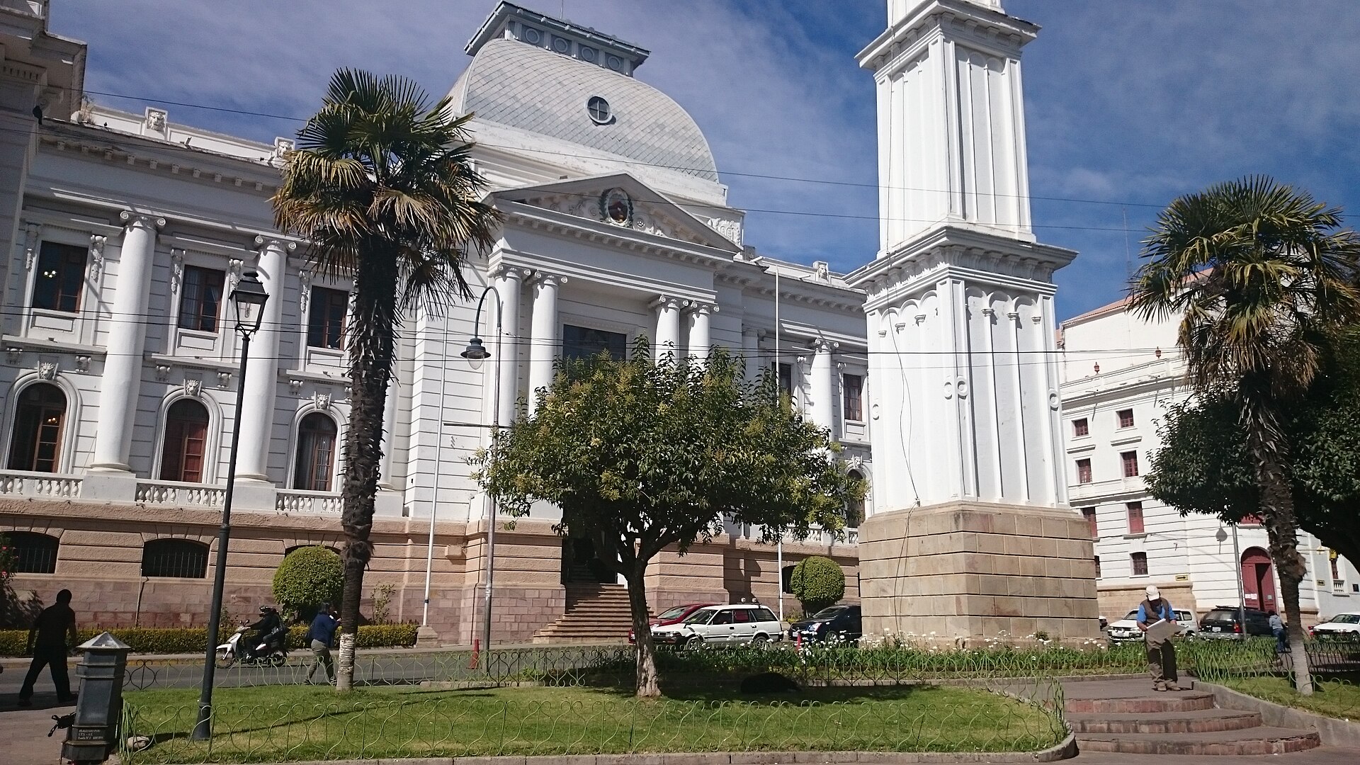 Neoclassical palace with a dome and a white bell tower beside palm trees on a plaza in Sucre, Bolivia