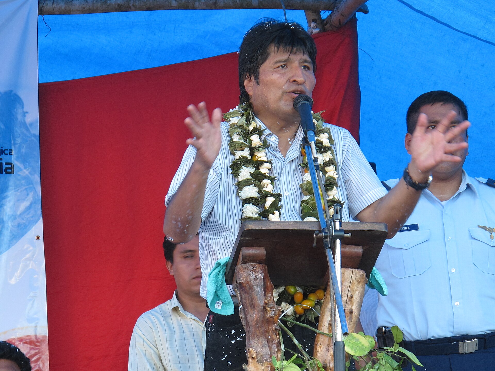 Evo Morales speaking at a lectern wearing a garland during an event in the Chapare, Bolivia