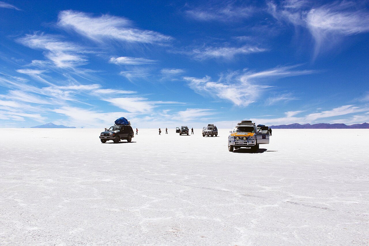 Tour jeeps and visitors on the flat white surface of the Salar de Uyuni under a blue sky