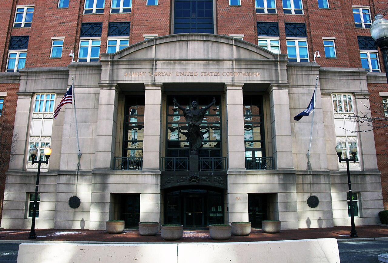 Stone entrance of the Albert V. Bryan United States Courthouse in Alexandria, Virginia, with a bronze statue above the doors and a US flag