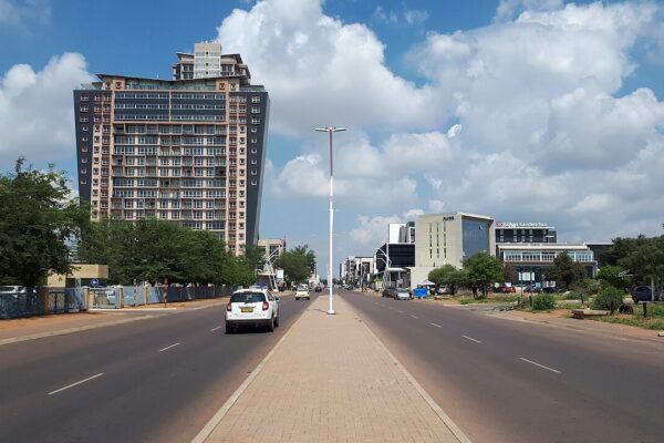 A wide street in Gaborone, Botswana, with a tall apartment tower and office buildings under a blue sky